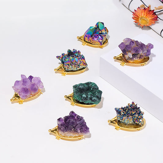 A group of decorative crystal hedgehog figurines with vibrant, glittering crystals on their backs, resting on golden bases. Each hedgehog features a unique crystal color and texture, including shades of purple, green, and iridescent hues. The arrangement on a clean, minimalist surface adds a whimsical and luxurious touch to these small, nature-inspired ornaments.